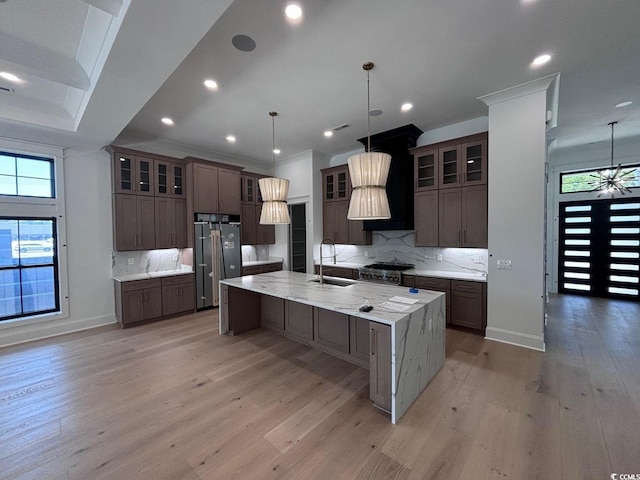 kitchen featuring a large island, high end refrigerator, a sink, light wood-type flooring, and baseboards