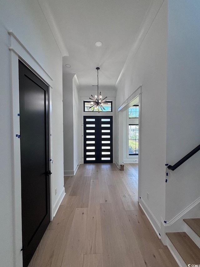 corridor featuring baseboards, a notable chandelier, light wood finished floors, and stairs