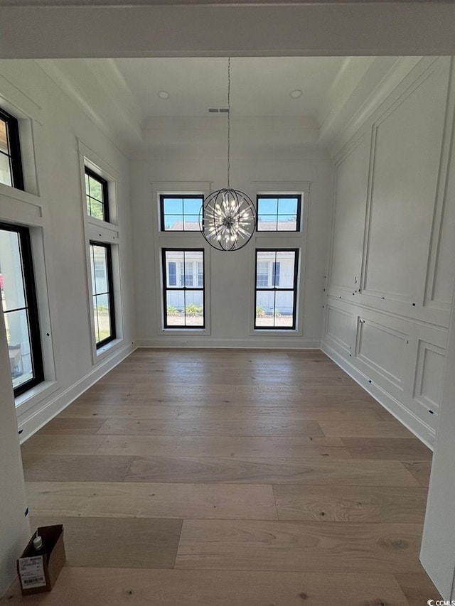 unfurnished dining area with light wood-type flooring, an inviting chandelier, and a towering ceiling