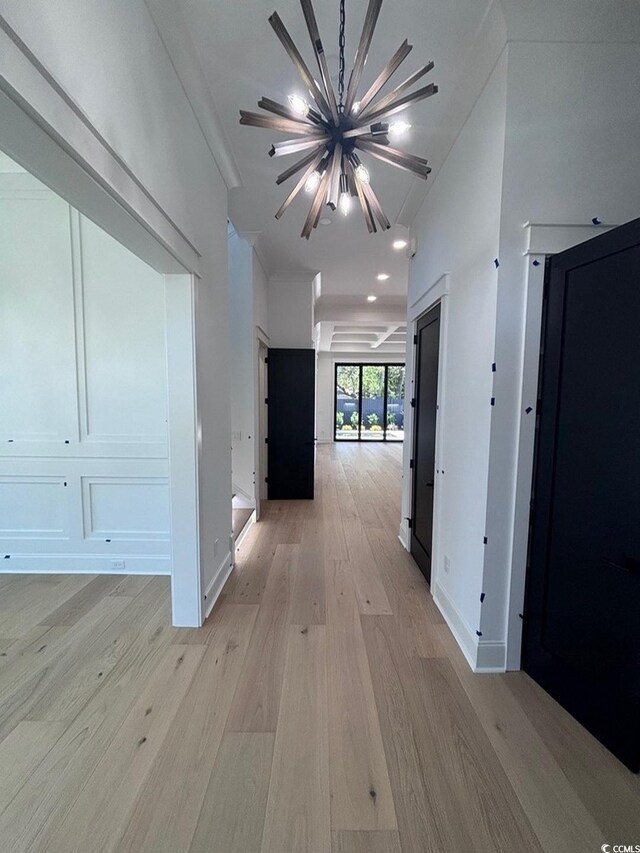 corridor featuring light wood-style flooring, a chandelier, and baseboards