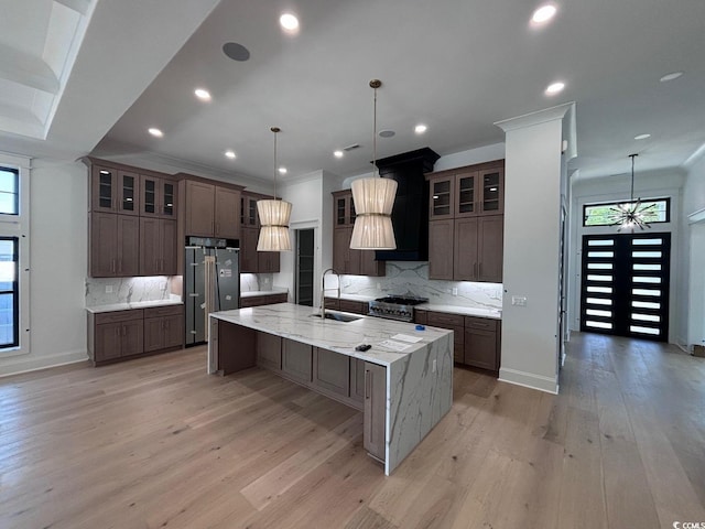 kitchen with a spacious island, a sink, backsplash, light wood finished floors, and high end appliances