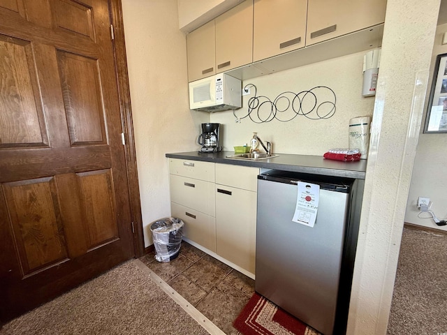 kitchen featuring white microwave, refrigerator, a sink, baseboards, and dark countertops