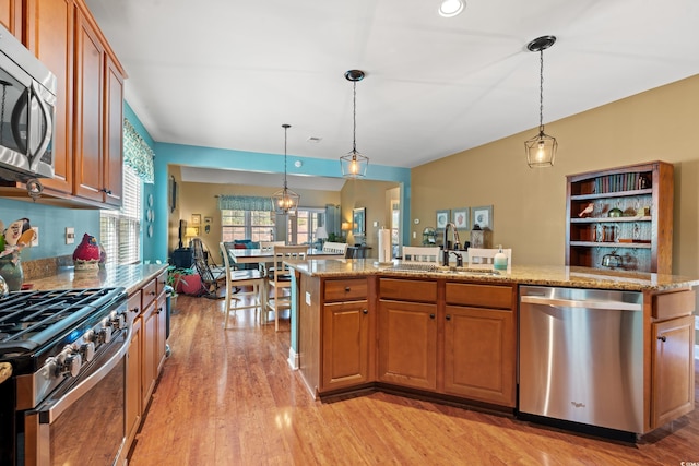 kitchen with light stone counters, light wood finished floors, stainless steel appliances, brown cabinetry, and a sink