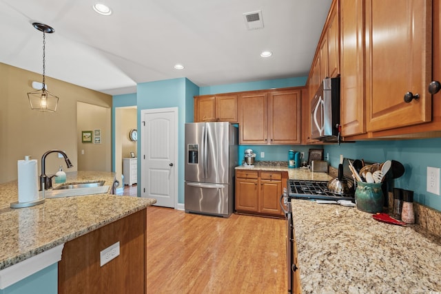 kitchen featuring brown cabinets, visible vents, appliances with stainless steel finishes, light wood-style floors, and a sink