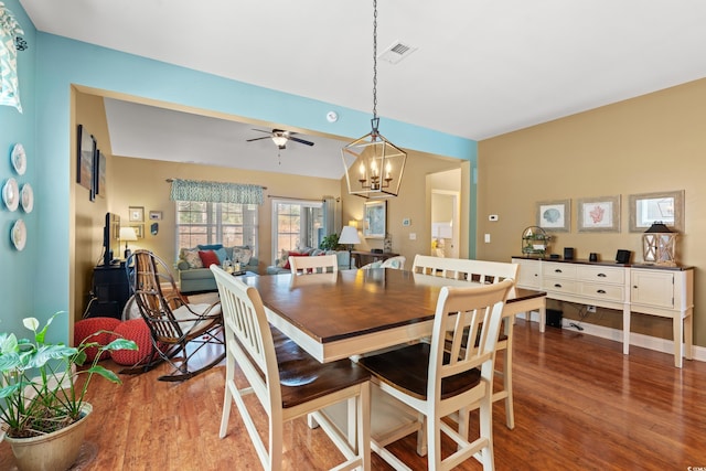 dining area featuring ceiling fan with notable chandelier, wood finished floors, visible vents, and baseboards