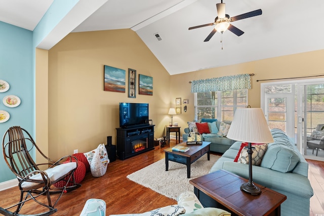 living area with ceiling fan, wood finished floors, visible vents, vaulted ceiling, and a glass covered fireplace