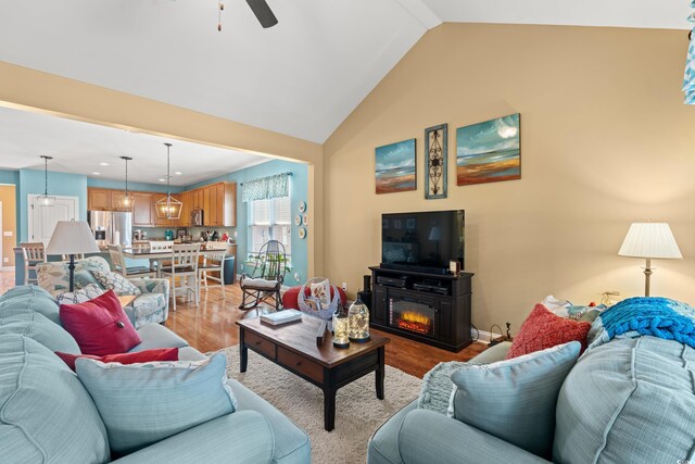 living room featuring light wood finished floors, a glass covered fireplace, vaulted ceiling, ceiling fan, and baseboards