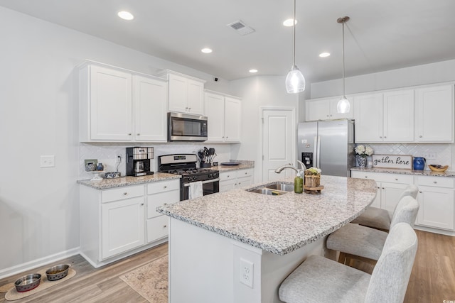 kitchen with a breakfast bar area, a kitchen island with sink, stainless steel appliances, a sink, and visible vents