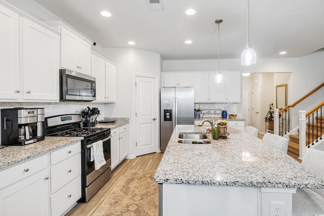 kitchen with light wood-style flooring, appliances with stainless steel finishes, a kitchen island with sink, white cabinetry, and a sink