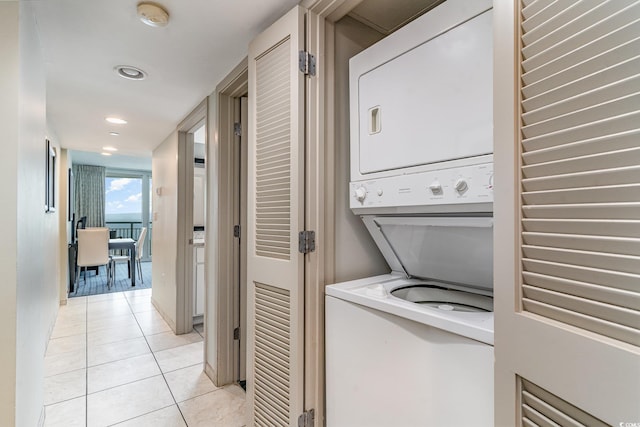 clothes washing area featuring stacked washer / dryer, laundry area, recessed lighting, and light tile patterned floors