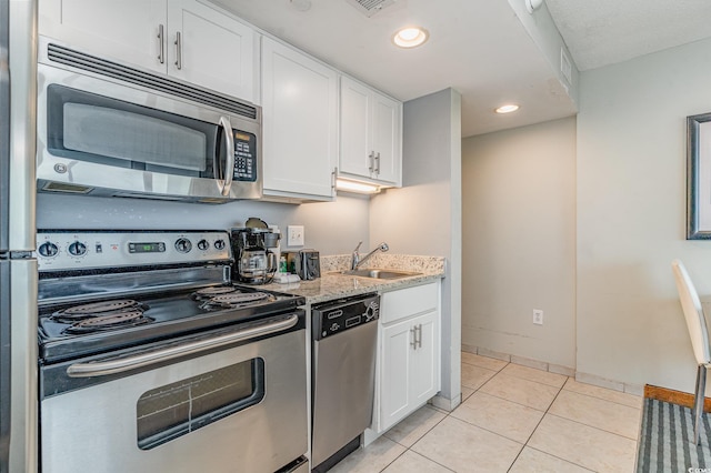 kitchen featuring light tile patterned floors, stainless steel appliances, white cabinetry, a sink, and light stone countertops