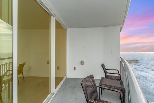 balcony at dusk featuring a water view