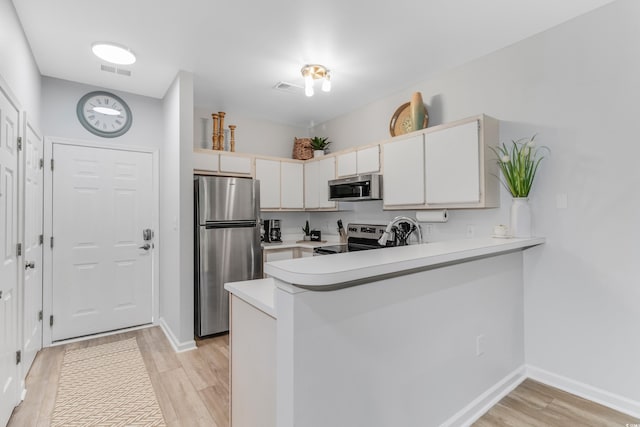 kitchen with a peninsula, light countertops, light wood-type flooring, and appliances with stainless steel finishes