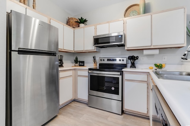 kitchen featuring light wood-type flooring, stainless steel appliances, light countertops, and a sink