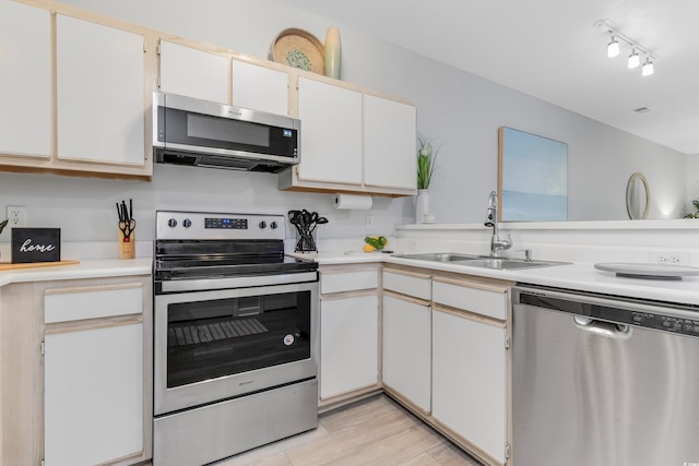 kitchen featuring track lighting, a sink, stainless steel appliances, light wood-style floors, and light countertops