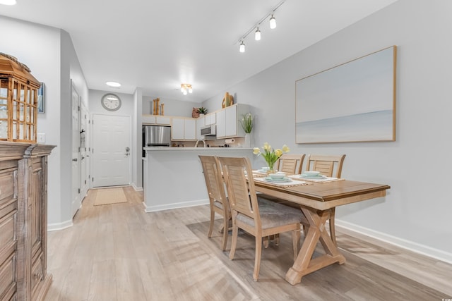 dining area with light wood-type flooring, baseboards, and rail lighting