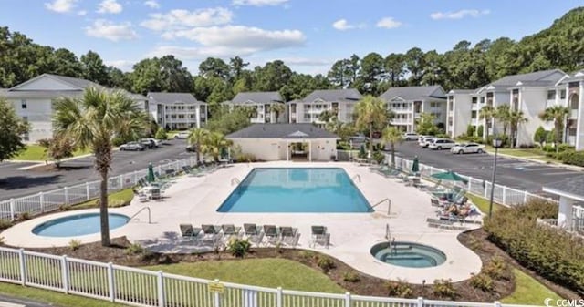 community pool with a residential view, a community hot tub, a patio, and fence