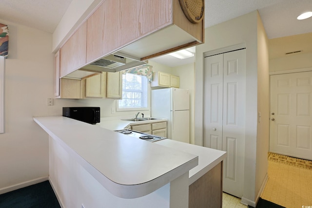 kitchen featuring a sink, freestanding refrigerator, a peninsula, light countertops, and light floors