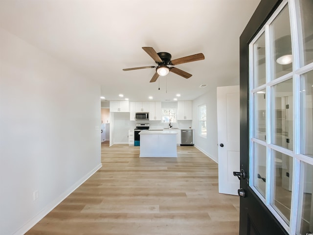 kitchen featuring a center island, stainless steel appliances, light wood finished floors, white cabinets, and baseboards