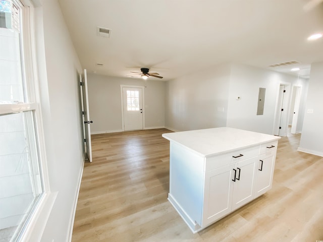 interior space with a center island, a ceiling fan, light wood finished floors, white cabinets, and baseboards