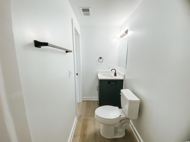 half bath with toilet, baseboards, visible vents, wood finished floors, and vanity