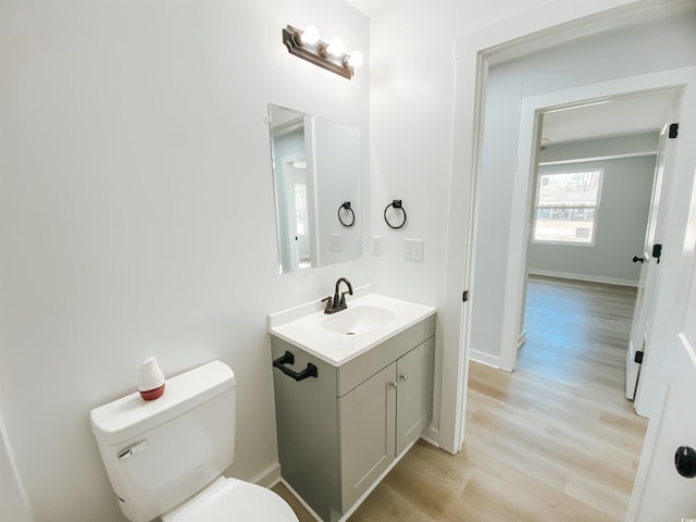 half bath featuring toilet, vanity, wood finished floors, and baseboards