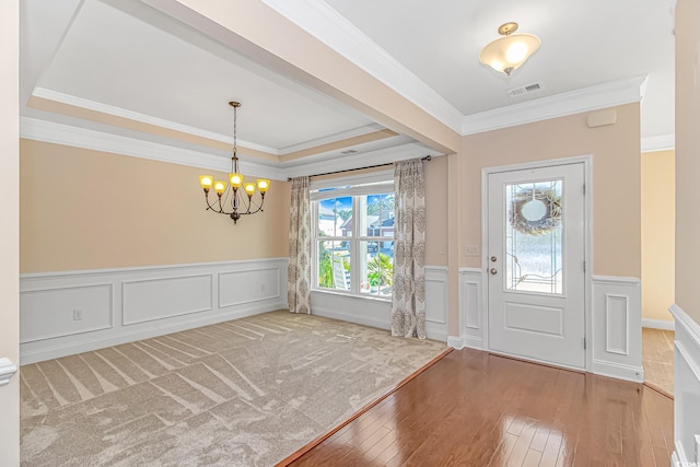 entryway with wood-type flooring, a chandelier, ornamental molding, wainscoting, and a raised ceiling
