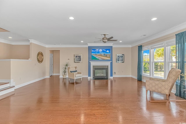 living area with a fireplace with flush hearth, ornamental molding, wood finished floors, and baseboards