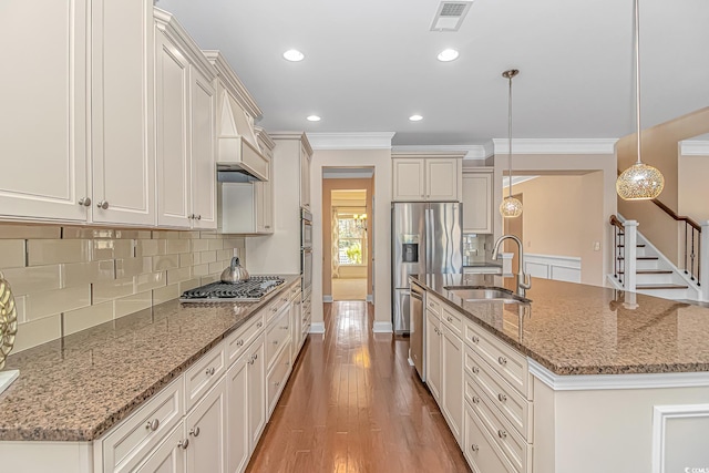 kitchen with a sink, stainless steel appliances, crown molding, decorative backsplash, and a center island with sink
