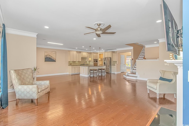 living area featuring light wood finished floors, stairs, a ceiling fan, and crown molding