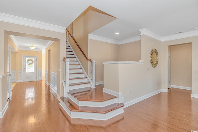 foyer featuring wood-type flooring, visible vents, a decorative wall, ornamental molding, and stairs