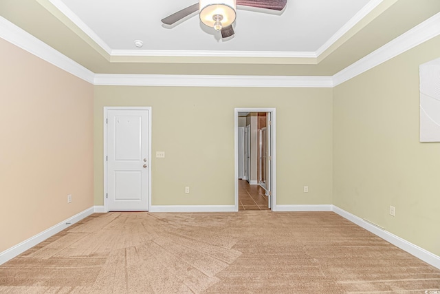 empty room with ceiling fan, light colored carpet, ornamental molding, a raised ceiling, and baseboards