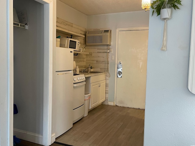 kitchen with a wall unit AC, white appliances, a sink, wood finished floors, and light countertops