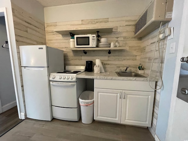 kitchen featuring white appliances, wooden walls, white cabinets, wood finished floors, and a sink