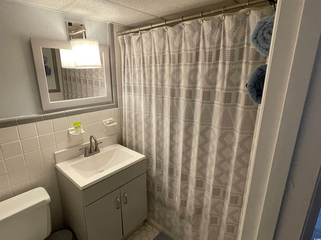 bathroom with a paneled ceiling, tile walls, toilet, and vanity