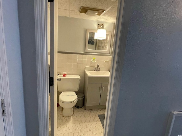 bathroom with tile patterned flooring, toilet, a wainscoted wall, vanity, and tile walls