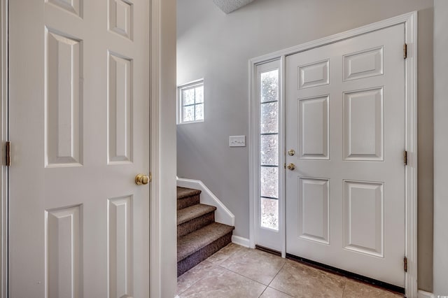 foyer featuring light tile patterned flooring, stairs, and baseboards