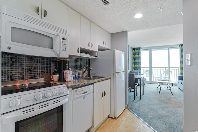 kitchen featuring light tile patterned floors, tasteful backsplash, light colored carpet, a sink, and white appliances