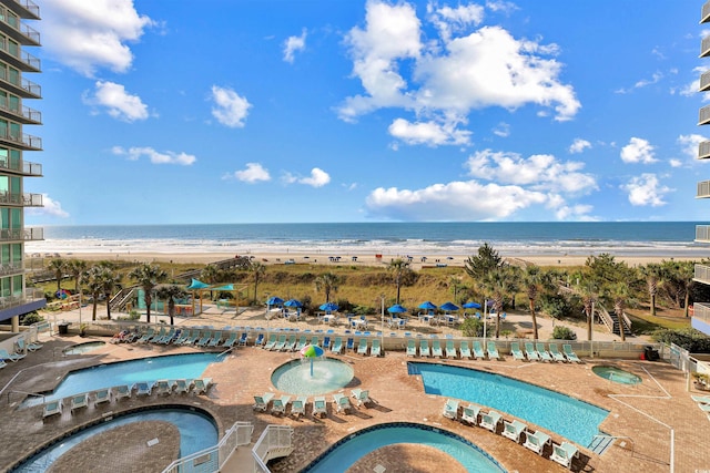 community pool featuring a view of the beach, a community hot tub, a patio area, and a water view