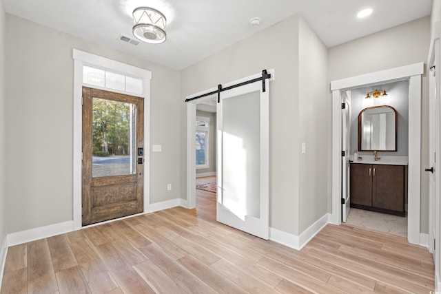 foyer entrance with light wood finished floors, a barn door, visible vents, and baseboards