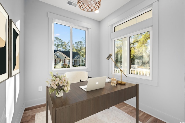 office space with wood finished floors, visible vents, and a healthy amount of sunlight