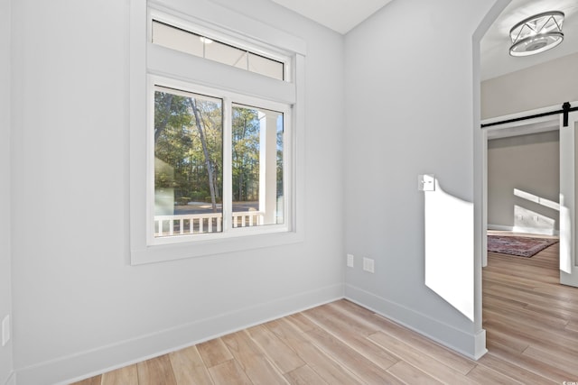 unfurnished room featuring light wood finished floors, baseboards, and a barn door