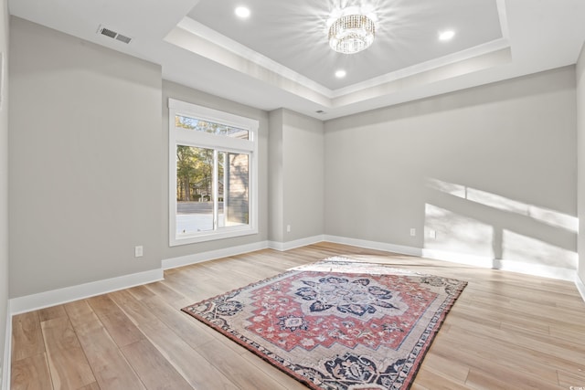 unfurnished room featuring a tray ceiling, recessed lighting, visible vents, wood finished floors, and baseboards