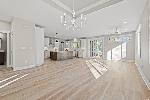 unfurnished living room featuring light wood-style flooring, ceiling fan with notable chandelier, baseboards, and recessed lighting