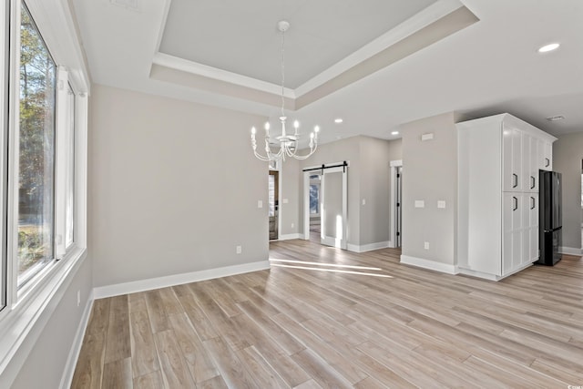 empty room with light wood finished floors, a tray ceiling, a barn door, and a healthy amount of sunlight