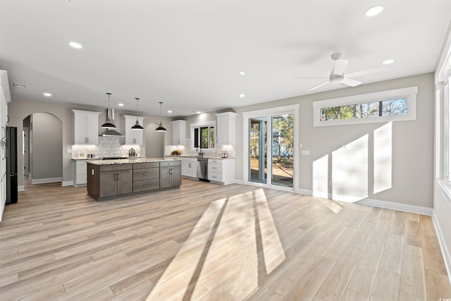 kitchen with arched walkways, decorative backsplash, light wood-style floors, dishwasher, and wall chimney exhaust hood