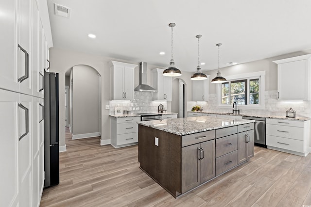 kitchen with arched walkways, a center island, a sink, dishwasher, and wall chimney exhaust hood