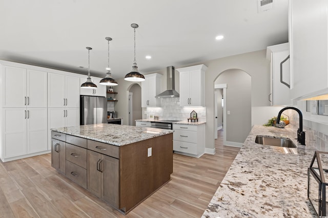 kitchen with arched walkways, decorative backsplash, freestanding refrigerator, a sink, and wall chimney exhaust hood