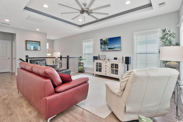 living room featuring a raised ceiling, visible vents, and plenty of natural light