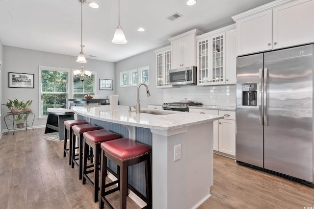 kitchen with light stone counters, white cabinets, light wood-style floors, appliances with stainless steel finishes, and tasteful backsplash